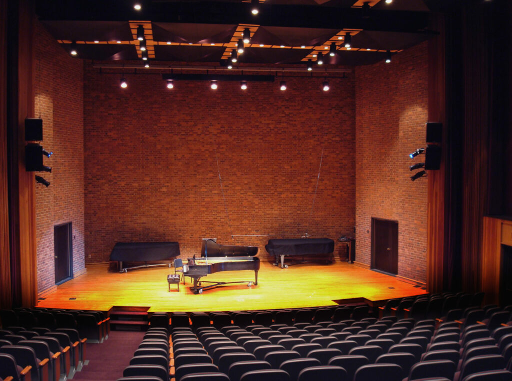 Empty recital hall with grand piano on stage.