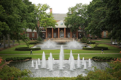 A grand fountain stands before the James B. Duke Library, complemented by greenery from nearby trees and bushes.